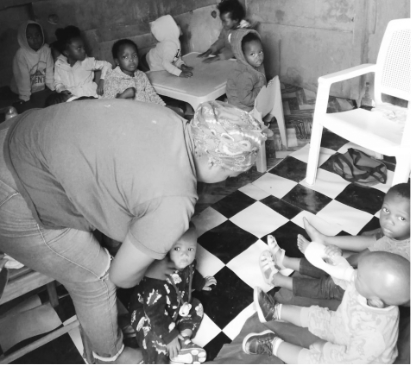 A volunteer interacting with children on a checkered playroom floor.